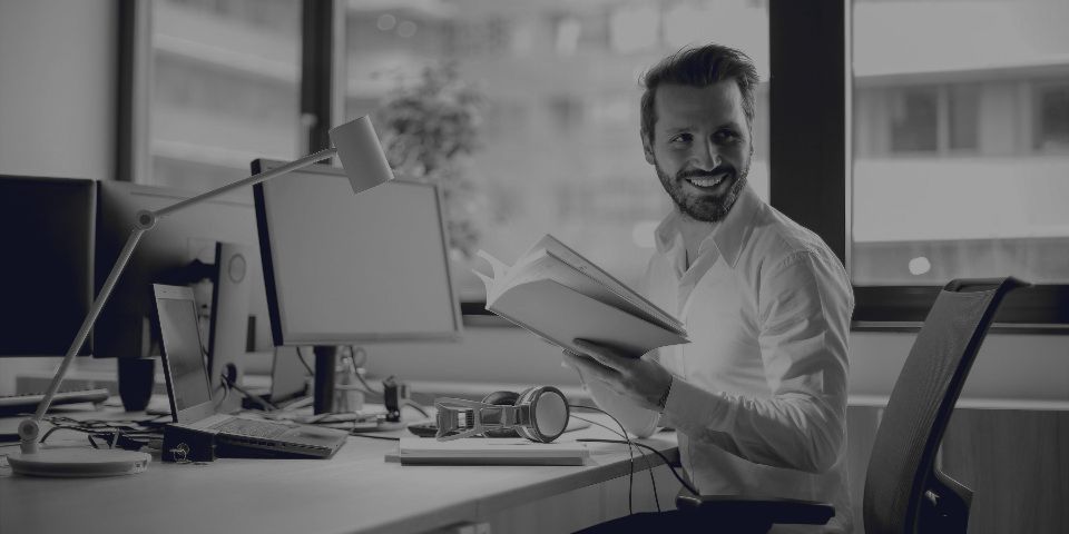A person smiling at their desk, an open folder in their hands.