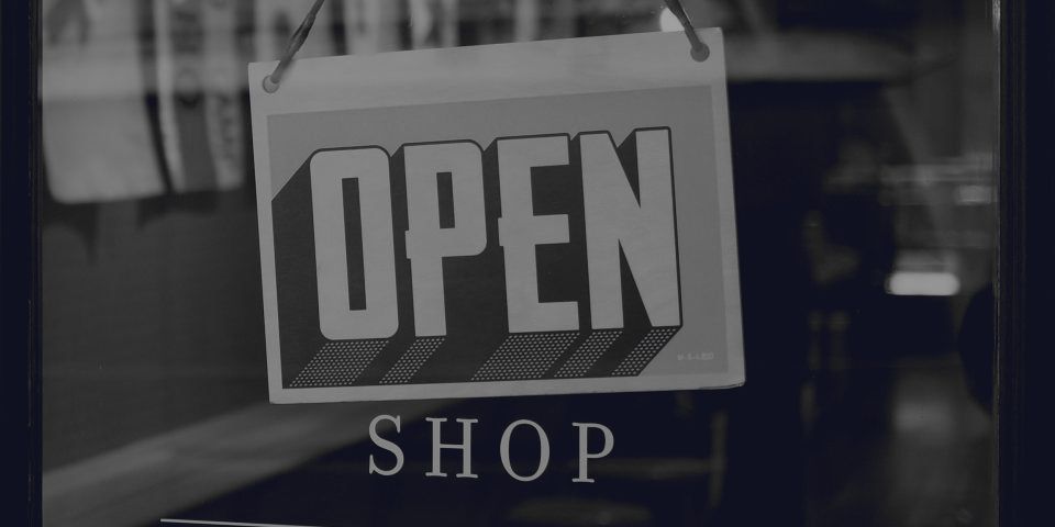 An “open” sign hanging in a shop window, the premises lit behind it.